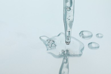 Photo of Glass pipette and transparent liquid on light background, closeup. Space for text