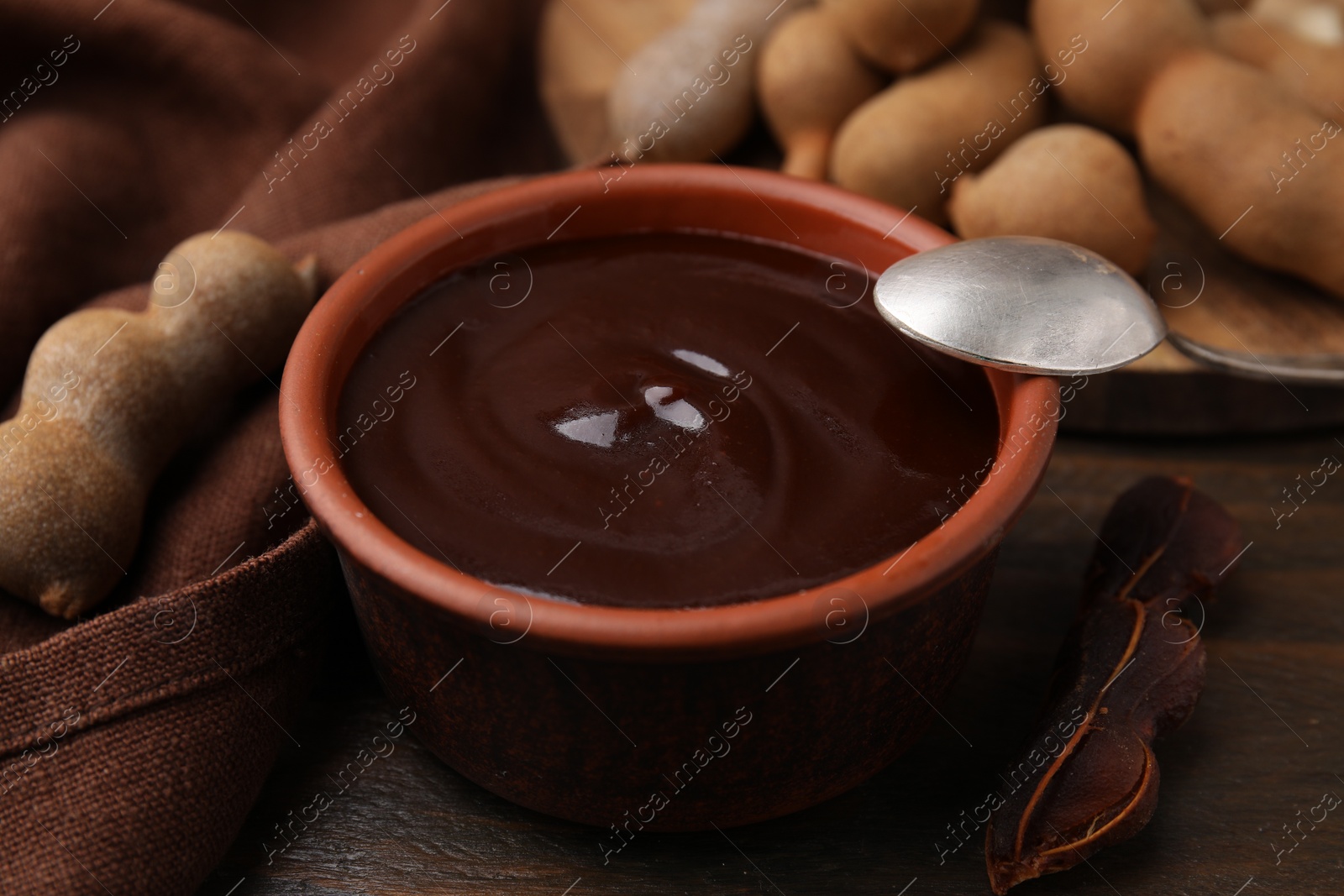Bowl of tamarind sauce, spoon and fresh pods on wooden table, closeup Photo of Bowl of tamarind sauce, spoon and fresh pods on wooden table, closeup