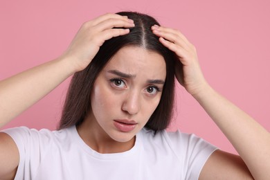 Photo of Sad woman examining her hair and scalp on pink background. Dandruff problem