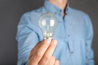 Photo of Man holding incandescent light bulb on grey background, closeup