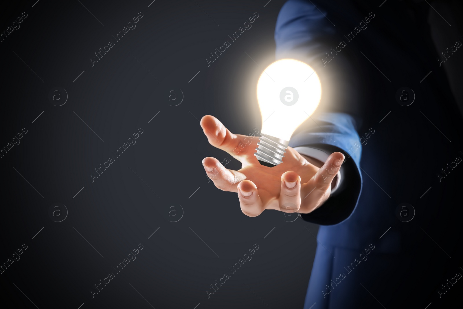 Image of Idea concept. Businessman demonstrating glowing light bulb illustration on dark background, closeup