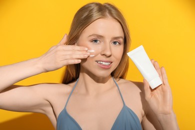 Beautiful young woman applying sun protection cream onto her face against orange background