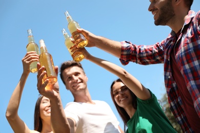 Photo of Young people holding bottles of beer against blue sky, focus on hands