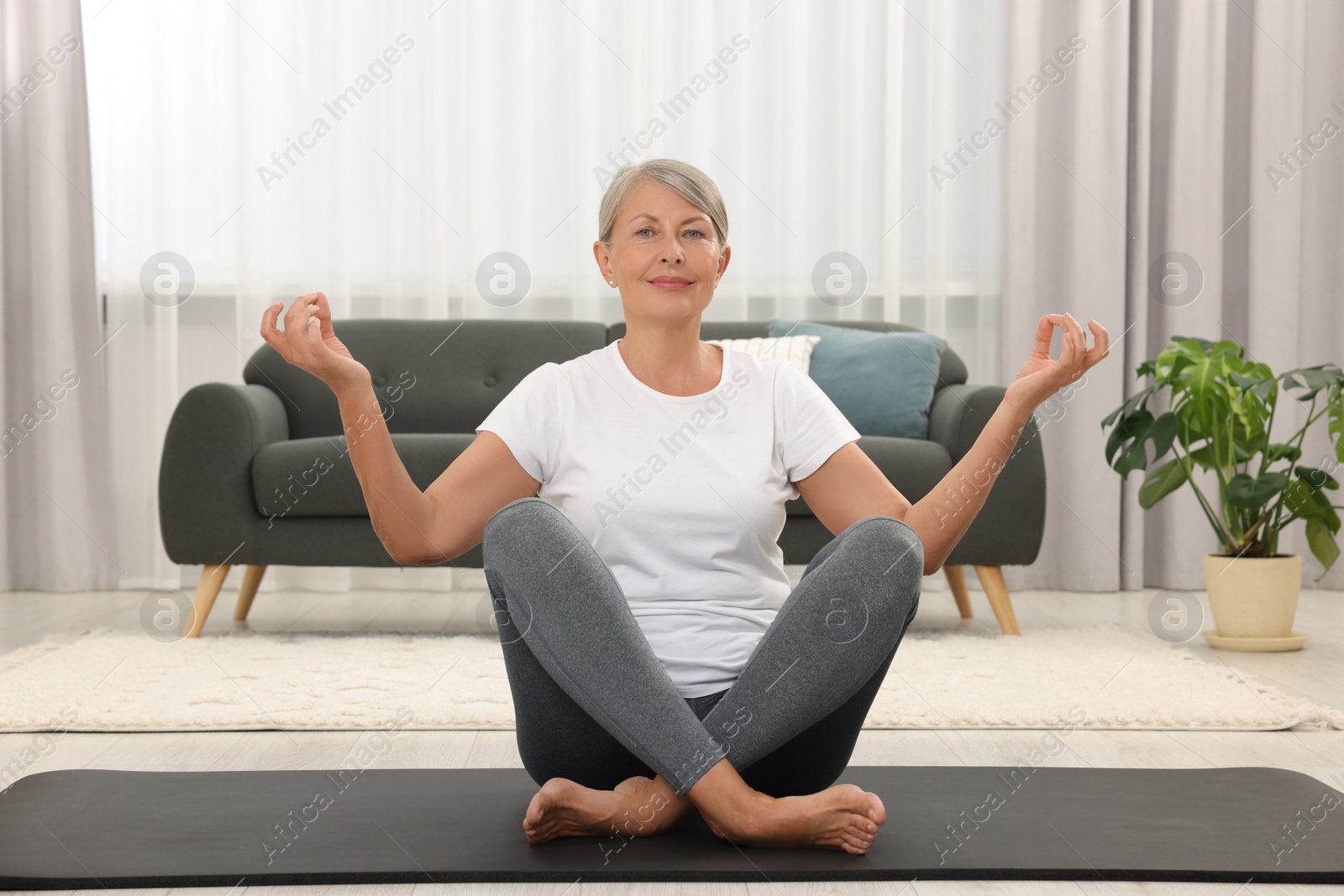 Photo of Happy senior woman practicing yoga on mat at home