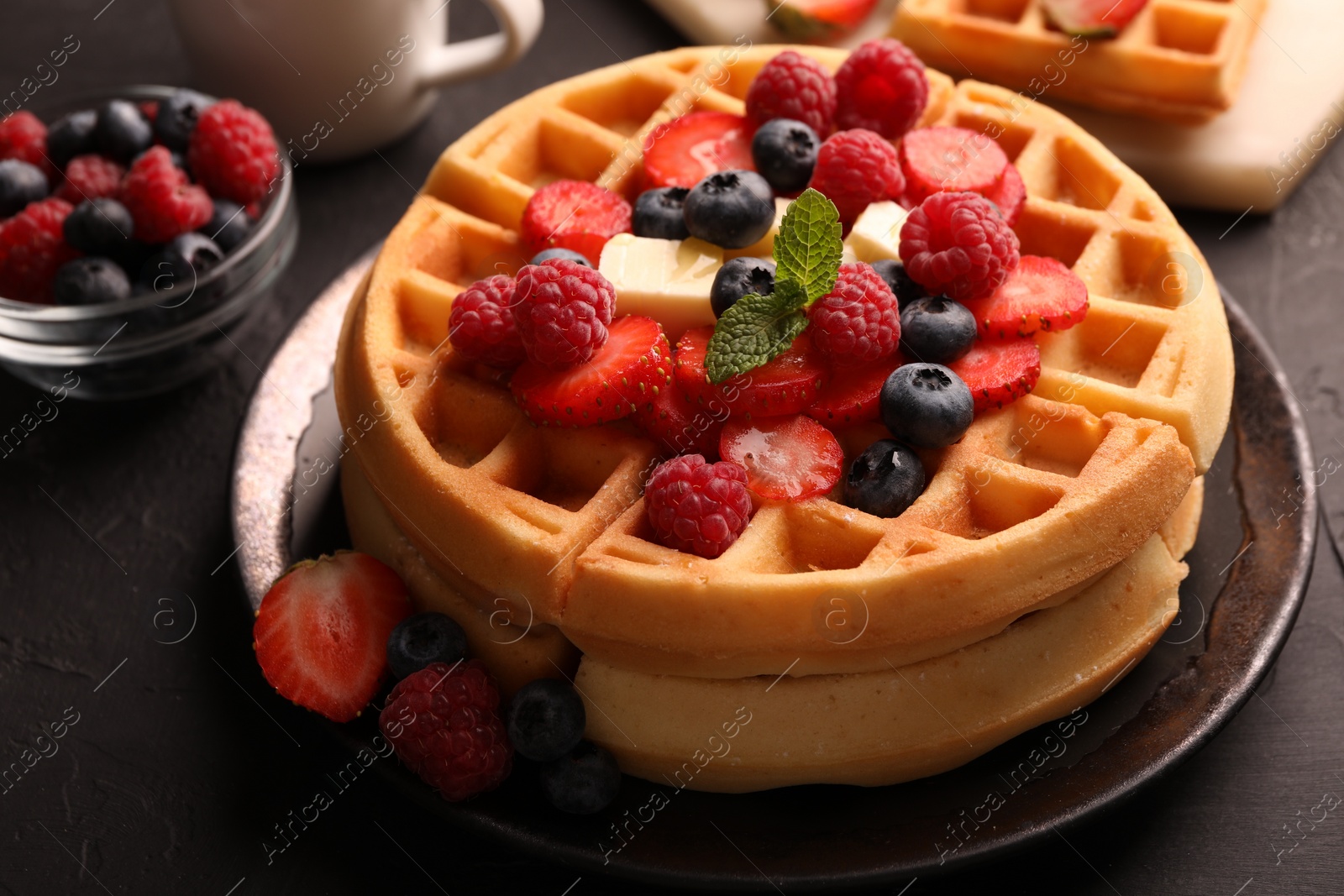 Photo of Tasty Belgian waffles with fresh berries and cheese on black table, closeup