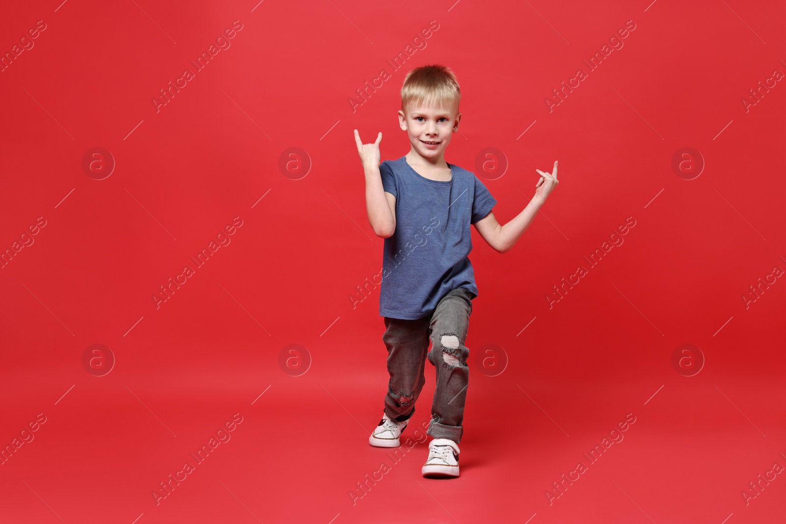 Photo of Happy little boy dancing on red background. Space for text