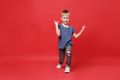 Photo of Happy little boy dancing on red background. Space for text