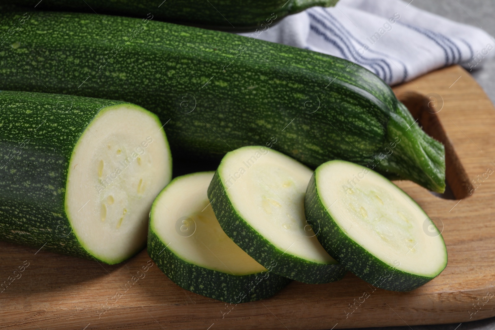 Photo of Whole and cut ripe zucchinis on wooden board, closeup