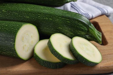 Photo of Whole and cut ripe zucchinis on wooden board, closeup