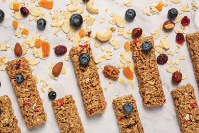 Photo of Tasty granola bars and ingredients on white marble table, flat lay