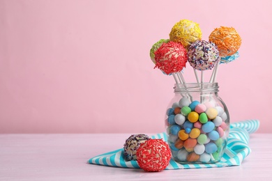 Glass jar with tasty cake pops and dragee on table against pink background, space for text