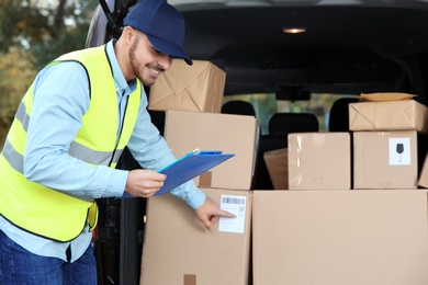 Photo of Young courier checking amount of parcels in delivery van, outdoors