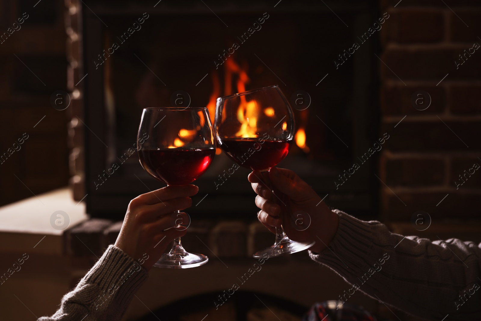 Photo of Couple with glasses of red wine near burning fireplace, closeup