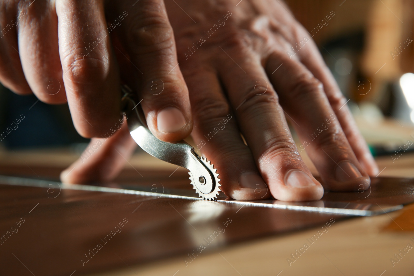 Photo of Man marking leather with roller in workshop, closeup