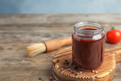 Photo of Composition with jar of barbecue sauce on wooden table. Space for text