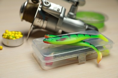 Different fishing baits and reel with line on light wooden table, closeup