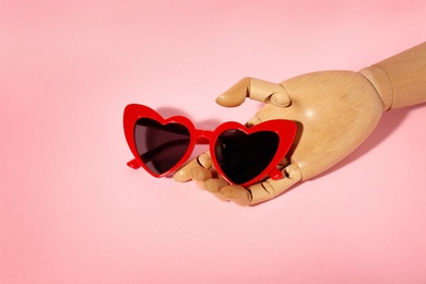 Wooden mannequin hand with stylish heart shaped glasses on color background