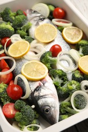 Raw fish with vegetables and lemon in baking dish on table