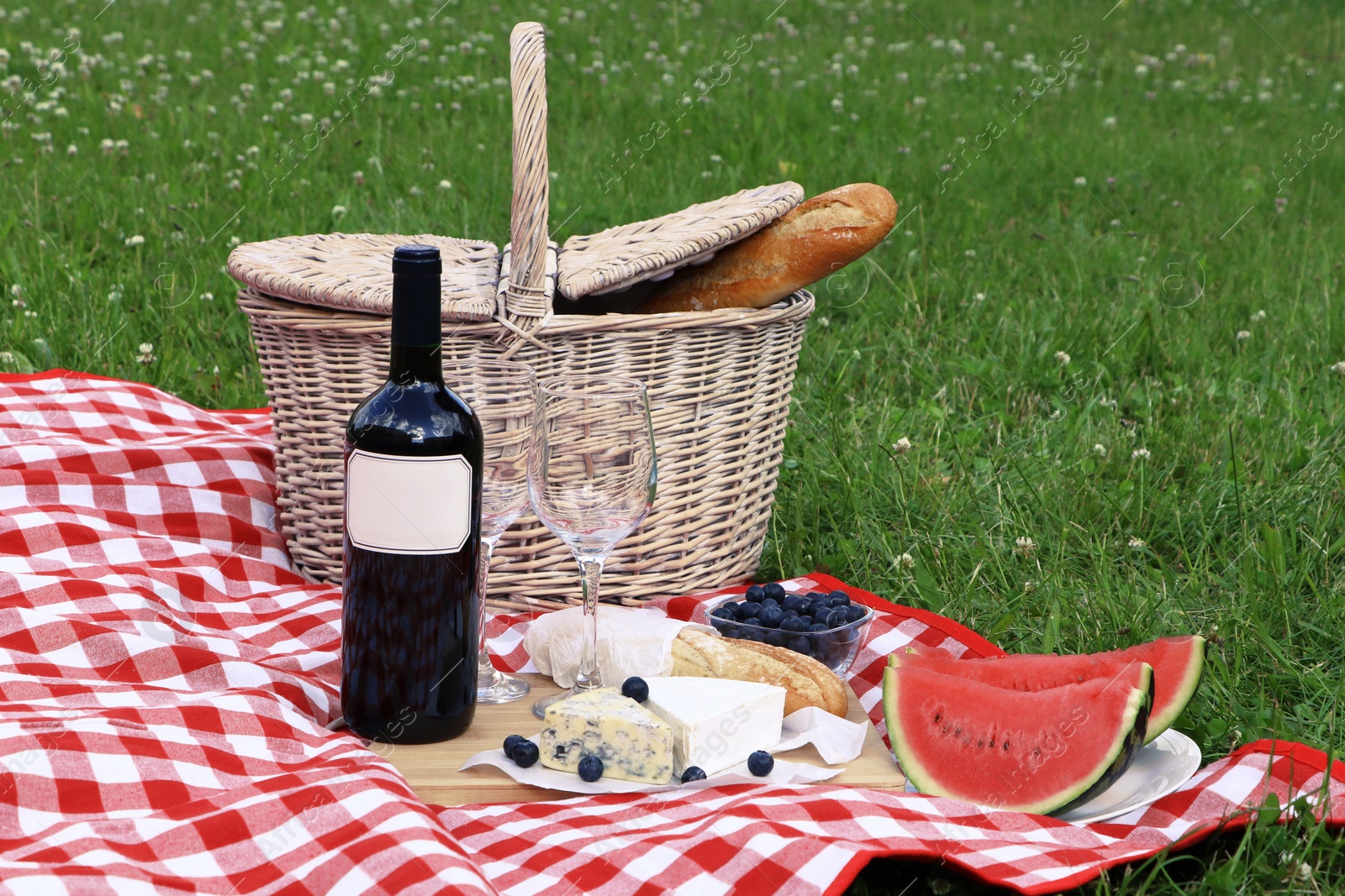 Photo of Picnic blanket with delicious food and wine outdoors on summer day