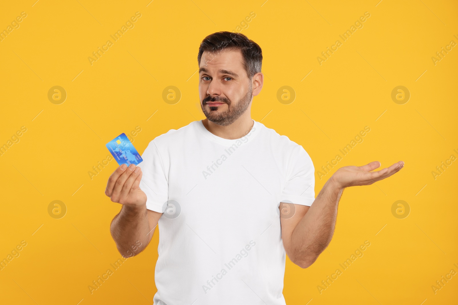 Photo of Confused man with credit card on orange background. Debt problem
