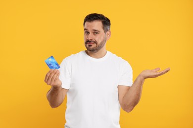 Photo of Confused man with credit card on orange background. Debt problem