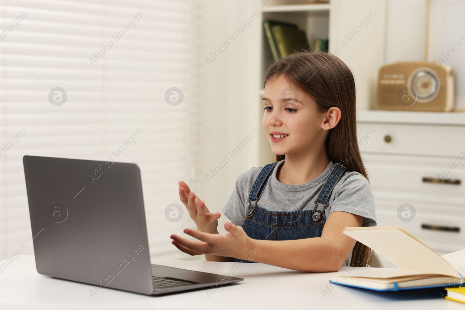 Photo of Cute girl having online lesson at white table indoors