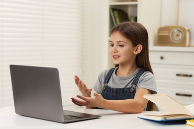 Cute girl having online lesson at white table indoors