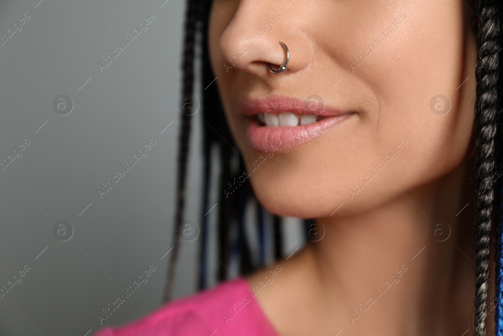 Photo of Young woman with nose piercing on grey background, closeup