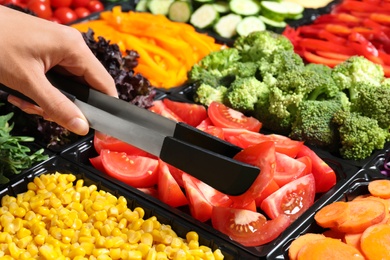 Photo of Young woman taking tomatoes from salad bar, closeup