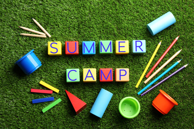 Photo of Flat lay composition with phrase SUMMER CAMP made of colorful cubes on green grass