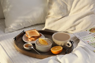 Photo of Wooden tray with delicious breakfast on bed in morning