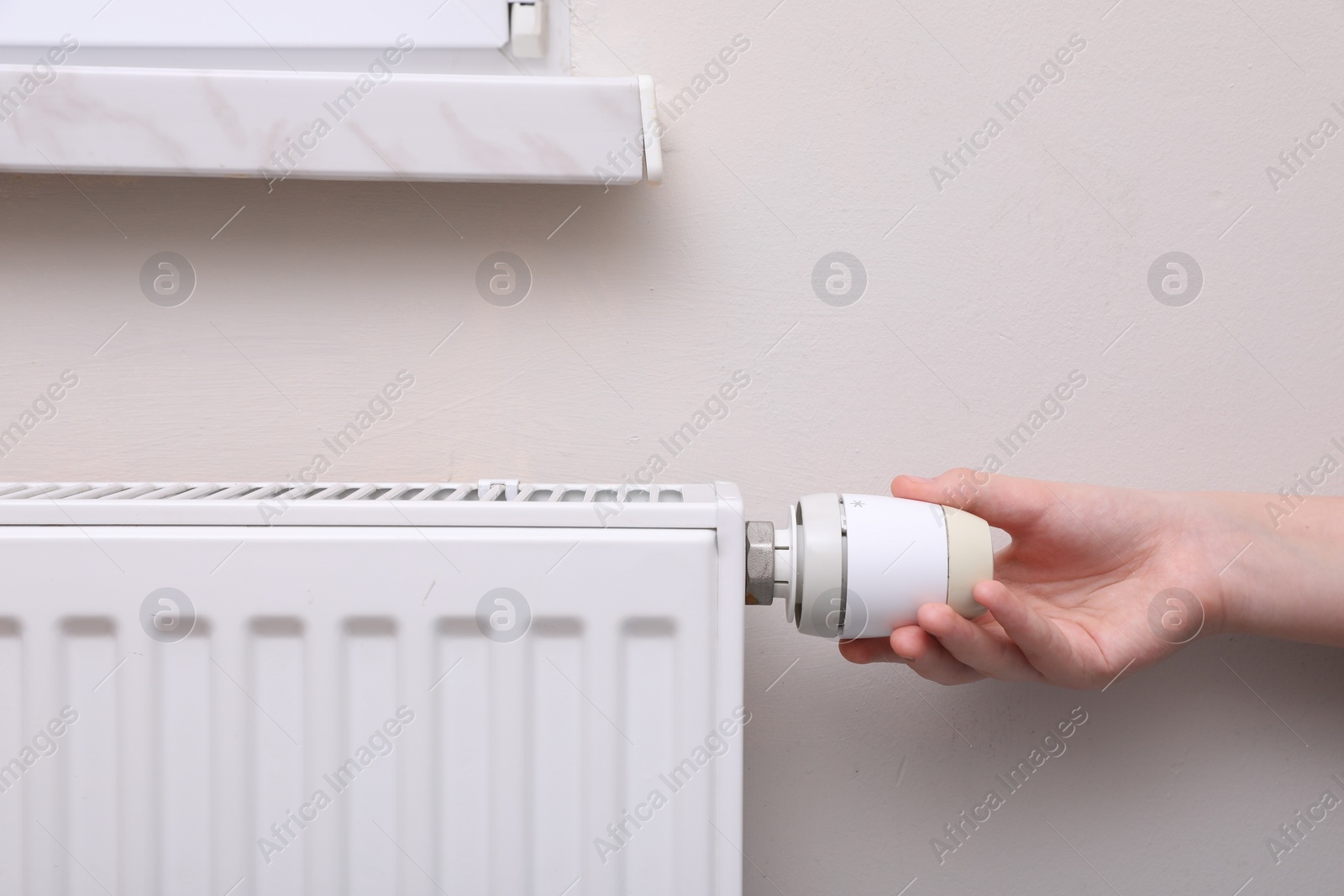 Photo of Girl adjusting heating radiator thermostat near white wall indoors, closeup