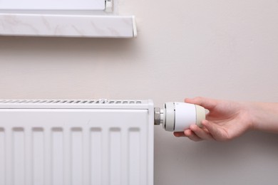 Photo of Girl adjusting heating radiator thermostat near white wall indoors, closeup