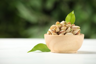 Photo of Tasty pistachios in bowl on white wooden table against blurred background, closeup. Space for text