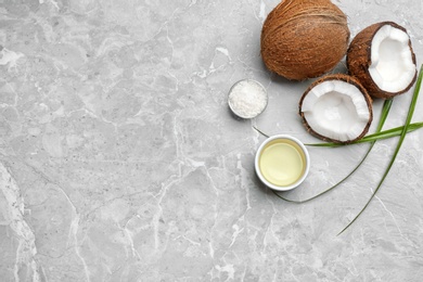 Photo of Bowl of natural organic oil and coconuts on grey stone background, flat lay. Space for text