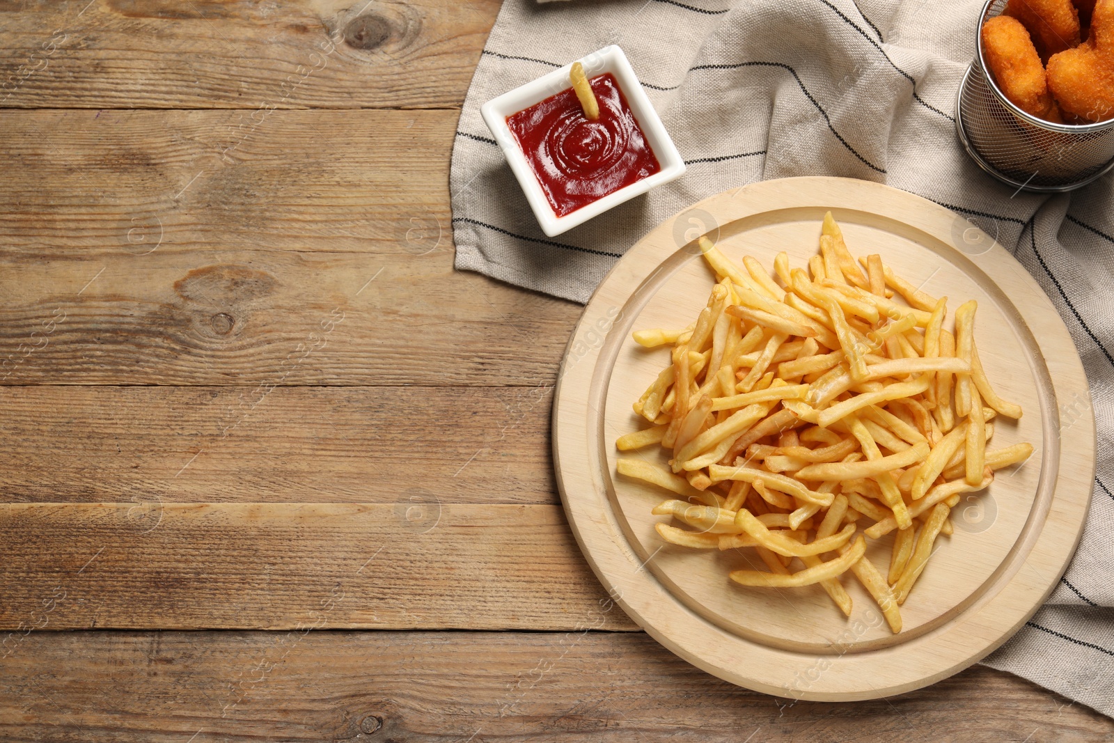 Photo of Tasty ketchup, fries and chicken nuggets on wooden table, flat lay. Space for text