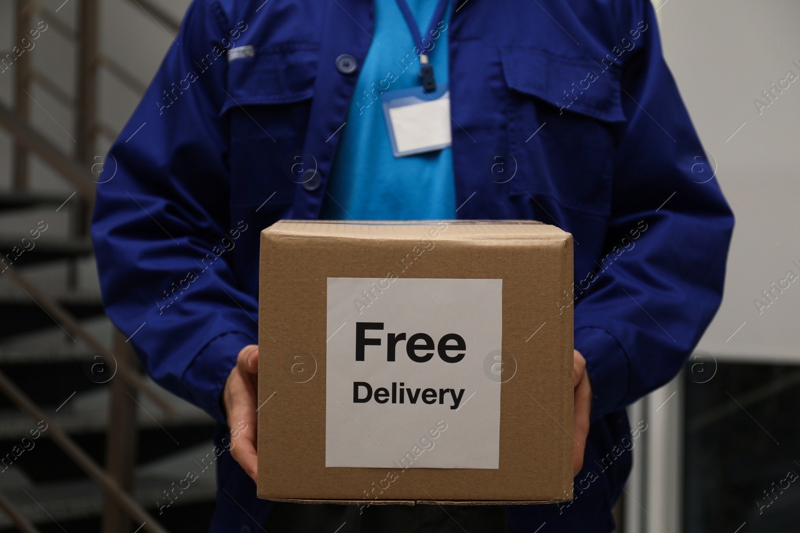 Photo of Courier holding parcel with sticker Free Delivery indoors, closeup