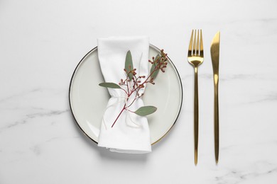 Stylish setting with cutlery and eucalyptus leaves on white marble table, flat lay