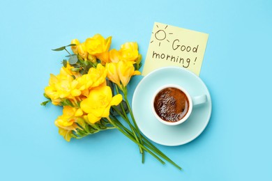 Photo of Cup of aromatic coffee, beautiful yellow freesias and Good Morning note on light blue background, flat lay