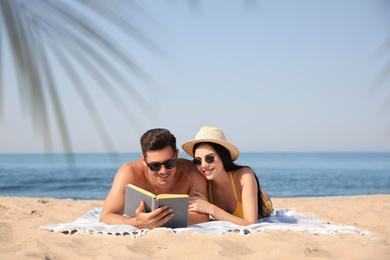 Photo of Happy couple reading book together on sunny beach