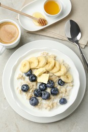 Photo of Tasty oatmeal with banana, blueberries, butter and milk served in bowl on light grey table, flat lay