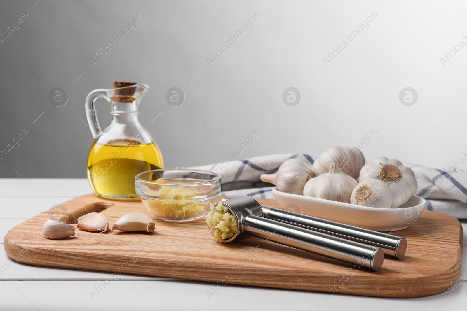 Photo of One metal press and crushed garlic on white wooden table