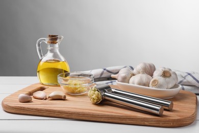 One metal press and crushed garlic on white wooden table