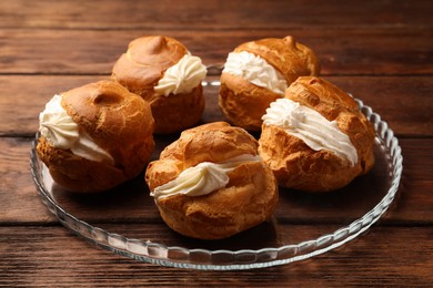 Photo of Delicious profiteroles with cream filling on wooden table