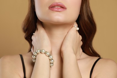 Young woman wearing elegant pearl jewelry on brown background, closeup