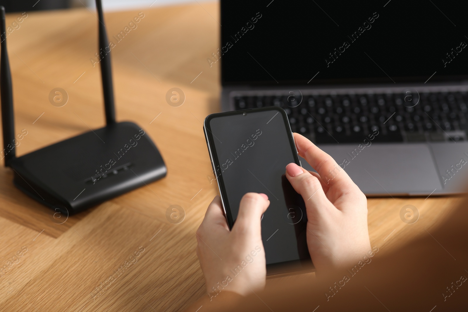 Photo of Woman with smartphone connecting to internet via Wi-Fi router at table indoors, closeup