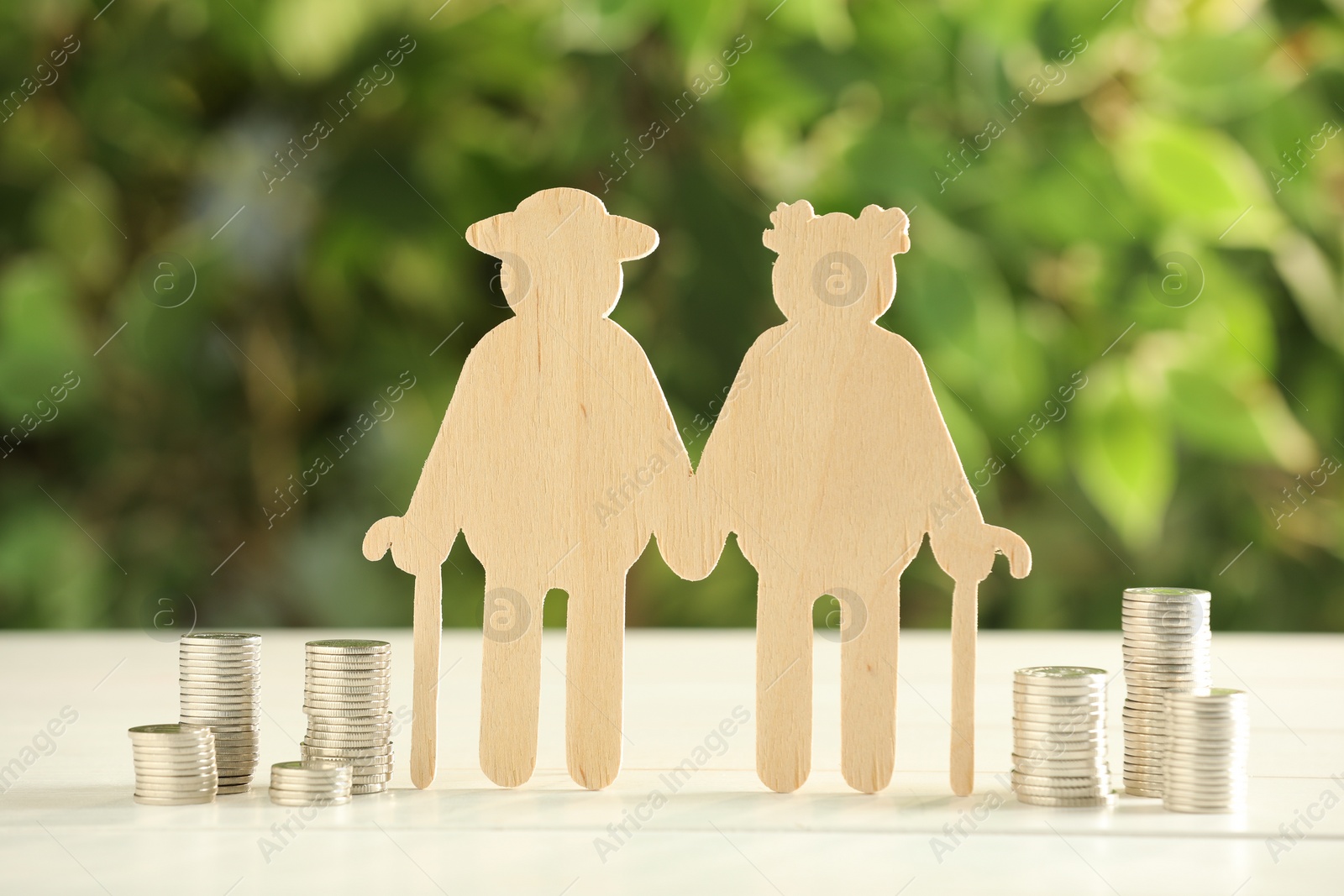 Photo of Pension savings. Figure of senior couple and stacked coins on white wooden table outdoors