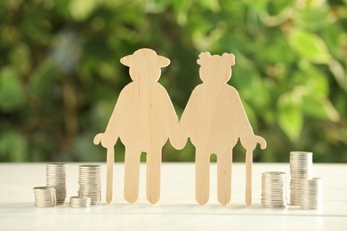 Photo of Pension savings. Figure of senior couple and stacked coins on white wooden table outdoors