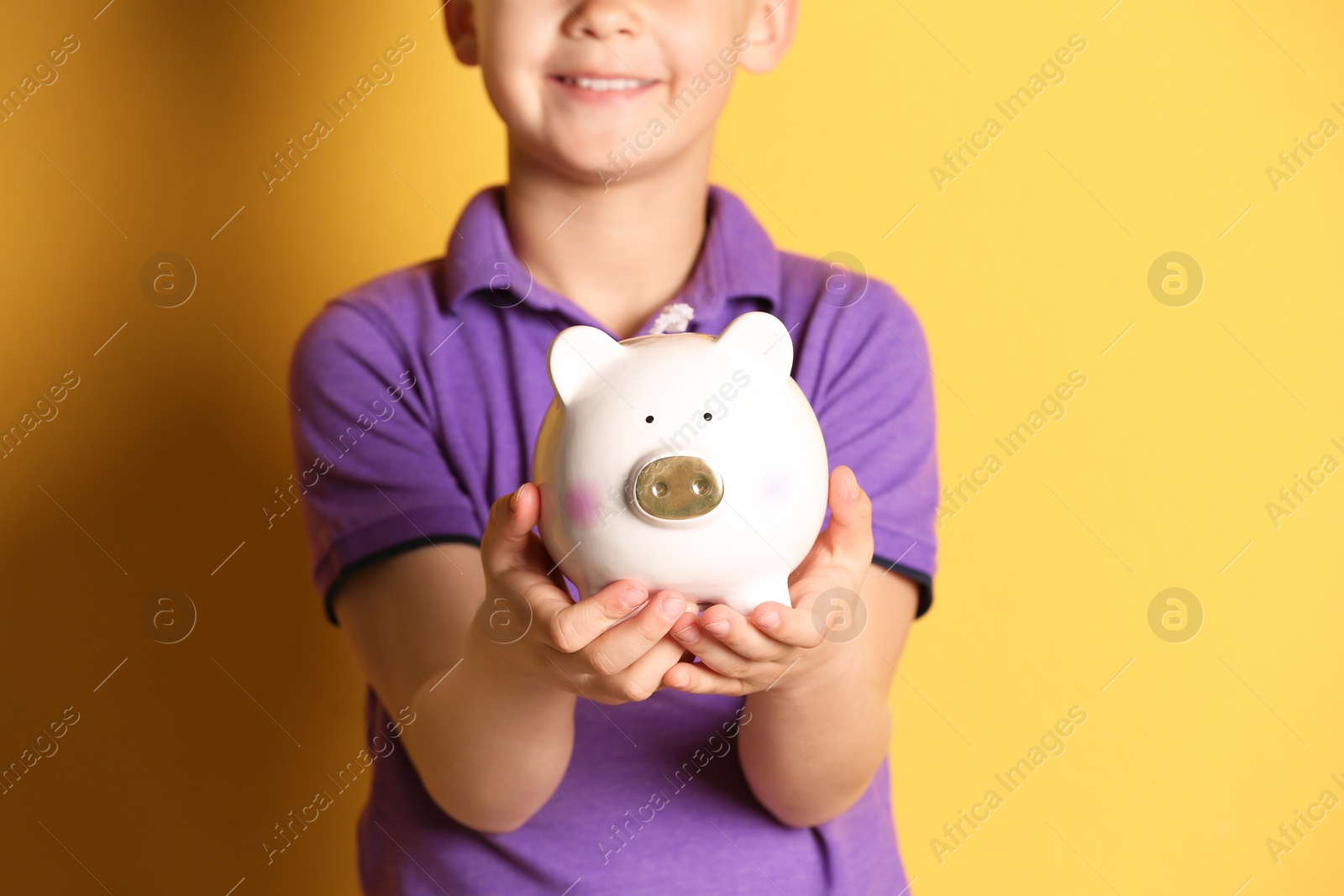 Photo of Little boy with piggy bank on color background, closeup