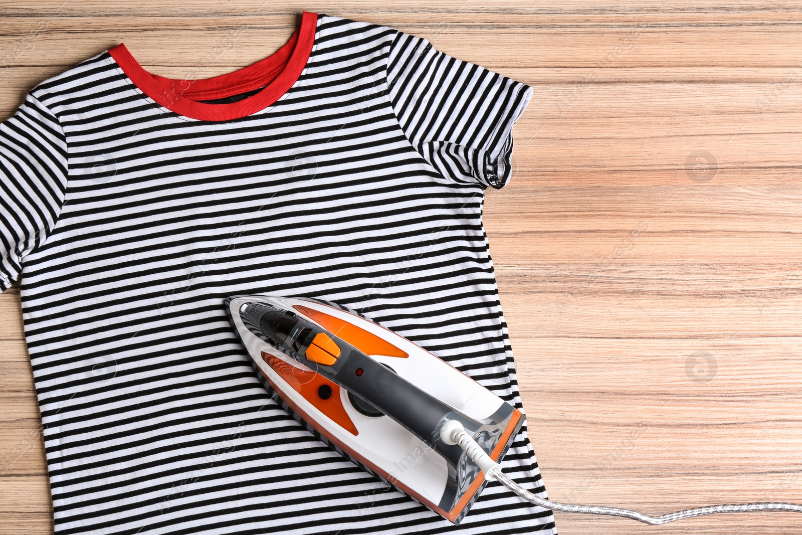 Photo of Flat lay composition with modern electric iron and t-shirt on wooden table. Space for text